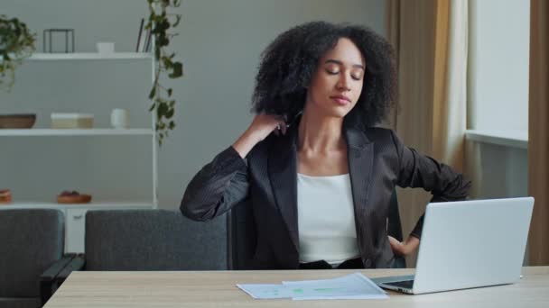若い民族アフリカ系アメリカ人女性従業員仕事残業コンピュータ上のオフィスで座っている不快な位置で筋肉のけいれん緊張を緩和疲れ過労女性の女の子マッサージバックリラックス体操 — ストック動画