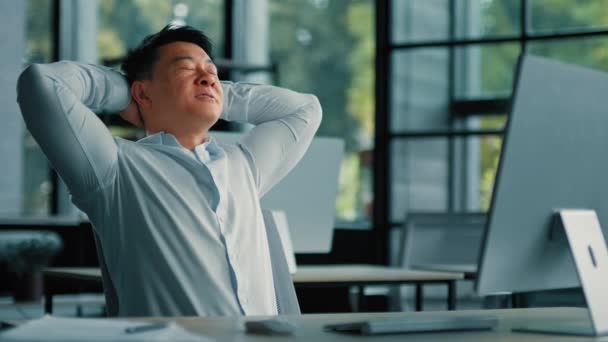 アジア系韓国人の先輩ビジネスマンが一人でリラックスオフィスチェアにもたれて頭の快適さの残りの部分の後ろに手を置くコンピュータの仕事に満足を感じる成功取引の後に休憩を取る仕事の日 — ストック動画