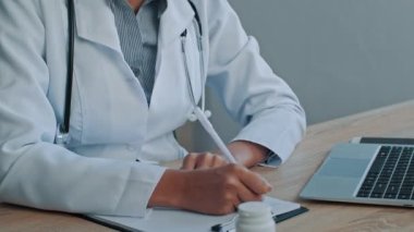 Terapist kadın pratisyen, maskeli Afrikalı kadın, hastane kliniğinde oturuyor, tedavi tarifi test sonuçları yazıyor, hastanın sağlık sigortalarını kontrol ediyor.