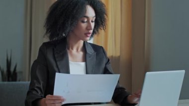 Afrikalı öğretmen, iş kadını, ofis kontrol belgelerinde grafik belgeleriyle çalışıyor. Bilgisayar bankacılığı uygulamasında faturaları öderken bilgisayardan bilgi işlemek için finansal veri girin.