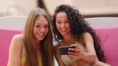 Güzel İspanyol beyaz kız arkadaşlar, bikini blogcu kadınlar yurtdışına seyahat ediyorlar, spa merkezinin güneşlendiği yerde güneşleniyorlar, video kullanımı, mobil telefon görüşmeleri, internet üzerinden keyifli sohbetler.