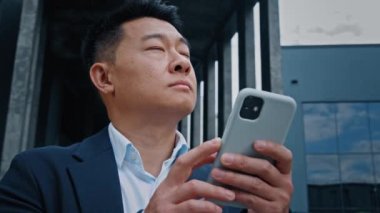 Kentteki 40 'lı yaşlardaki Koreli iş adamını cep telefonu yazma, taksi rezervasyonu, sohbet akıllı telefon Asyalı girişimciyle mesajlaşma ve düşünceli düşünce çevrimiçi harita kontrolü kullanarak kapatın.