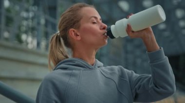 Yorgun bayan sporcu atletik beyaz kız koşucu genç spor model kadın stadyum vücut bakımı hidratında spor üstüne enerji için sağlıklı içecekler içiyor.