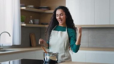 Enerjik, şakacı, aktif Arap kadın ev hanımı, 30 'lu yaşlarda anne dansçı, modern mutfak dansında aile için yemek pişiriyor, evde tek başına yüksek sesli müzik dansı, aşçılık hobisini harekete geçiriyor.