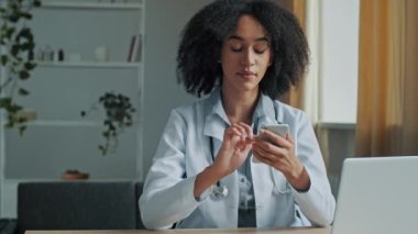 Afrikalı doktor kadın terapist cep telefonu uygulaması kullanıyor. Hasta danışmanlığı için tıbbi mesajlar yolluyor. Salgın zamanlarında, modern teknoloji ve sağlık hizmetleri için online mesafe tedavisi öneriyor.