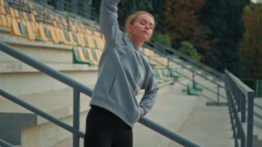 Aktif sporcu kadın, spor yapan beyaz kadın stadyumda kaslarını esnetiyor. Spor yapan genç kız, kollarını kaldırıyor. Sabah yogaya meyilli, açık havada kilo verme egzersizi yapıyor.