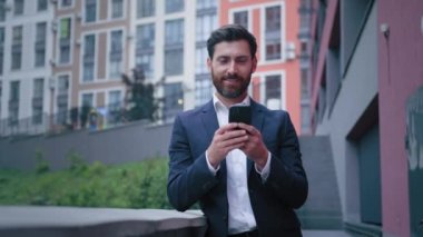 30 'lu yaşlardaki başarılı beyaz erkek işadamı sakallı yetişkin adam akıllı telefondan sohbet ediyor mobil bildirim okuyor ofis dışındaki alet telefonuyla internet uygulaması kullanıyor.
