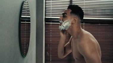 Banyoda dans eden adam mutlu İspanyol adam aynaya bakıyor köpük krem sürüyor tıraş oluyor jel dansı yapıyor komik işaret parmaklarıyla yansımaya işaret ediyor