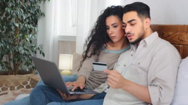 Evli çift, karı koca müşteriler yatak odasında alışveriş yapıyor internet mağazasından alışveriş yapıyor dizüstü bilgisayarla alışveriş yapıyor banka kredi kartıyla e-ticaret sipariş ediyor.