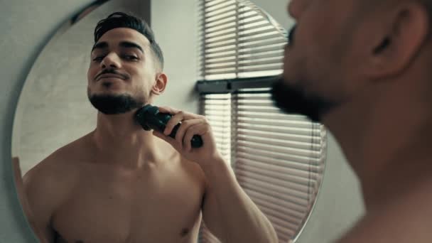 洗澡间镜子中的男装倒影 不刮胡子 在家里刮脸 一个英俊的30多岁的拉丁裔男人留着胡子的西班牙男人用电动剃须刀刮胡子 — 图库视频影像