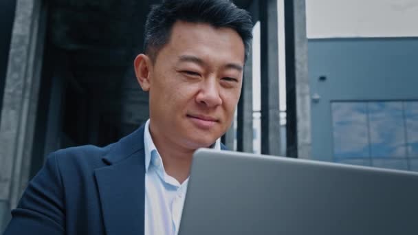 幸せな笑顔正の韓国語40代の中高年実業家弁護士フリーランスの投資家雇用主の起業家は コンピュータと都市の男で屋外ノートパソコンを入力オンラインプロジェクトで笑顔の成功 — ストック動画