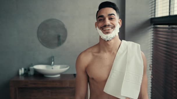 浴室里有趣的男性画像拉丁男人在刮胡子前摆出笑脸 西班牙裔印度人笑得很开心 性感的男人留着胡子 脸上带着洁白肥皂泡 刮胡子胶 保持浴巾卫生 — 图库视频影像