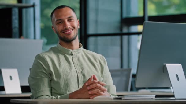 快乐微笑的男性投资人多种族开发人员程序员创意设计师非裔美国人办公室里拿着电脑看着镜头微笑坐在公司工作场所的桌子旁 — 图库视频影像