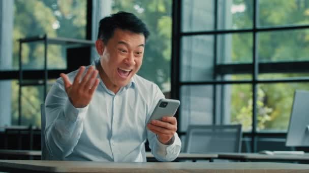 驚いたアジアの成功したビジネスマンの感情的な男のプロの勝者は携帯電話で良いメッセージを受け取るショックはすごい成功を祝うと言うオンラインベット収益性の高いオファーの給与 — ストック動画