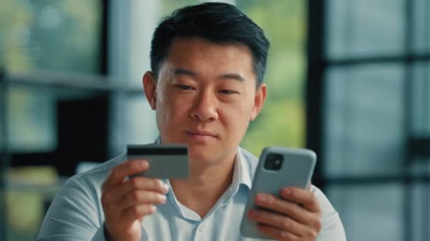 幸せなアジアの男性の顧客バイヤービジネスマンオフィスで銀行の携帯電話アプリを使用プラスチッククレジットカードを保持インターネットストアで安全なコードを入力オンラインショッピングで商品を購入暗号通貨マネー取引 — ストック動画