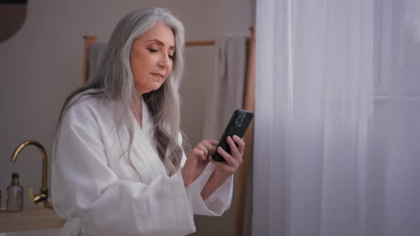 Évek Öreg Kaukázusi Idősebb Nagymama Áll Fürdőszobában Fürdőköpenyben Nézi Telefonkönyv — Stock videók