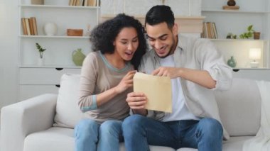 Hintli Latin kökenli, çok ırklı evli çift, etnik bir aile kadını ve karı koca kanepede oturup banka bildirimi okuyarak piyango parası kazanırlar.