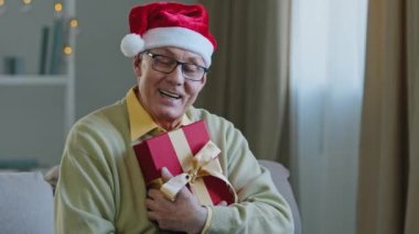 Yaşlı, beyaz, yetişkin, gözlüklü, Noel Baba şapkalı, kırmızı şapkalı, dedesi koltukta oturan 60 'lı yaşlarda bir adam.