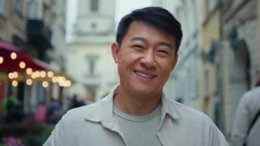 Kameraya bakıp gülümseyen dost canlısı bir erkek turist yeni şehirleri ziyaret ediyor tatilin keyfini çıkarıyor mutlu bir müşteri hafta sonu tatili tatilinin tadını çıkarıyor Asya modelinin yakın plan pozlarını veriyor.