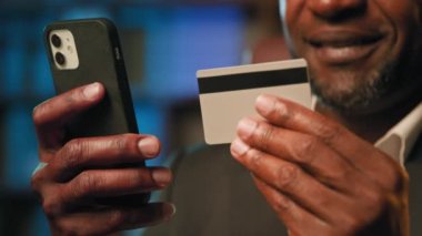 Yakın plan erkek eli kredi kartı ve telefon sahibi tanınmayan adam online mağazadan uzaktan alışveriş yapıyor. Mobil bankacılık uygulaması güvenli mesafe ödemesi modern teknoloji konseptini kullanıyor.