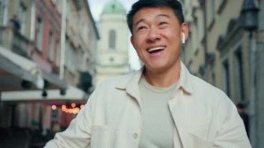 Neşeli adam kablosuz kulaklıkla müzik dinliyor açık havada dans eden Asyalı erkek turist ritmik olarak favori şarkıya geçiyor mp3 'ün tadını çıkarıyor ve dinamik sokak dansı yapıyor.
