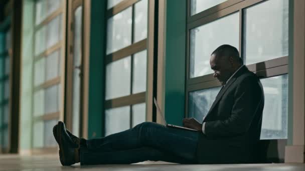 パズルに焦点を当てた成熟したアフリカ系アメリカ人男性が床の上に座っているラップトップの上に入力男性作家ジャーナリスト記事を書き込みます無料のWifiビジネスマンフリーランサーインターネット締め切りコンセプトに関するレポートを作成 — ストック動画