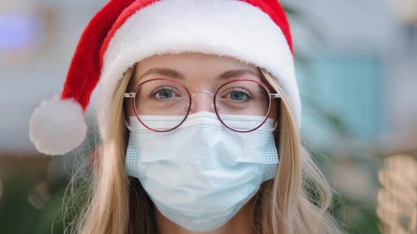 閉じるまで女性のポートレート白人女性女性女性看護師医師身に着けています赤サンタクリスマス帽子キャップと眼鏡と保護医療面マスク新年XmasパンデミックコロナウイルスCovid病気 — ストック動画