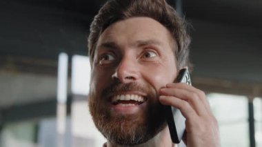 Aşırı yakın plan erkek yüzü Kafkas sakallı, 40 'lı yılların girişimcisi telefonla konuşan, uzaktan konuşan, gülümseyen, telefon eden sanal görüşmeleri yapan mutlu iş adamı ofisteki akıllı telefonuyla konuşuyor.