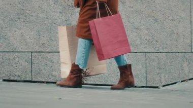 Alışveriş yaptıktan sonra sokakta yürüyen tanınmayan bir kadın. Kot pantolonlu, kahverengi ayakkabılı ve ceketli bir kadın. Şehirdeki bilinmeyen bir müşterinin elinde alışveriş merkezinden alınmış kese kağıtları var. Kara Cuma.