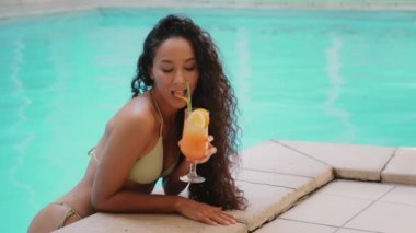 Seksi güneşlenen bayan yüzücü turist Arap kökenli Latin kökenli seksi bronzlaşmış kadın spa kompleksinin yüzen havuzunda egzotik kokteyl içiyor neşeli bir gülümsemeyle yaz tatilinin tadını çıkar.