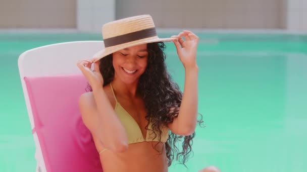 在豪华酒店游泳池附近 身着帽子日光浴的西班牙千禧年女模特在日光浴中摆姿势 摆姿势拍照 调侃音乐 享受暑假 — 图库视频影像