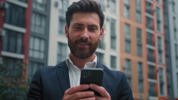 白人ハンサムなプロフェッショナルビジネスマン中年男性ホールド携帯電話ガジェット仕事オンラインで市内屋外チャット上の携帯電話読み取りSms使用電子銀行アプリEコマース現代的な技術コンセプト — ストック動画
