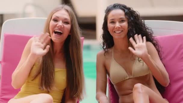 两位年轻女士穿着比基尼的美丽的女性博主女友在网上记录旅行美丽视频博客 她们挥手向游客问好 并在游泳池附近的热带度假胜地度过暑假 — 图库视频影像