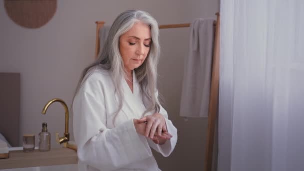 美しいおばあちゃん60代の女性高齢者白髪の女性ベッドルームで白人女性摩擦しわ手適用自然手クリーム保湿腕若返り美容手順健康スキンケア — ストック動画