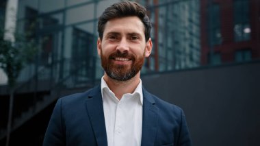 Yakışıklı, beyaz sakallı, 40 'lı yılların iş adamı patronu başarılı, erkek iş adamı mutlu, yetişkin bir adam modern ofis şirketinin önünde durmuş neşeli bir gülümsemeye bakıyor.