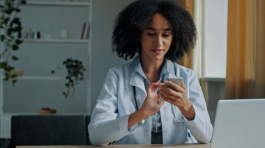 Afrikalı doktor kadın terapist cep telefonu uygulaması kullanıyor. Hasta danışmanlığı için tıbbi mesajlar yolluyor. Salgın zamanlarında, modern teknoloji ve sağlık hizmetleri için online mesafe tedavisi öneriyor.