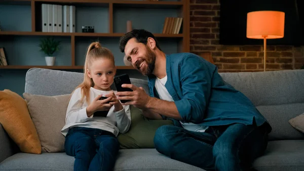 白人男人和小女孩一起坐在家里拿着现代电话浏览媒体内容在线游戏成人爸爸教女儿用移动应用程序在无线设备上播放有趣的视频 — 图库照片
