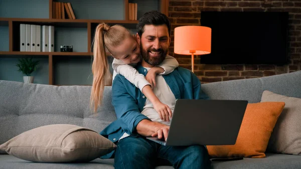 Cute active naughty girl noisy child plays with daddy hugs father distract parental attention disturbs parent from work on laptop at home single loving caucasian dad man calms down restless daughter