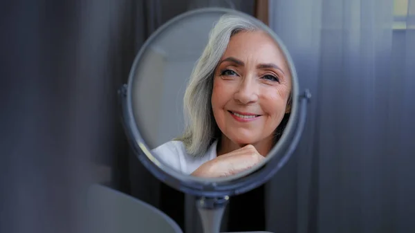 美しい女性の顔を笑顔50中年の成熟した女性は 鏡の反射緩和を見て顔の皮膚をお楽しみください 古い老化乾燥したスキンケア美容手順化粧品アンチエイジングプラスチック手術 — ストック写真
