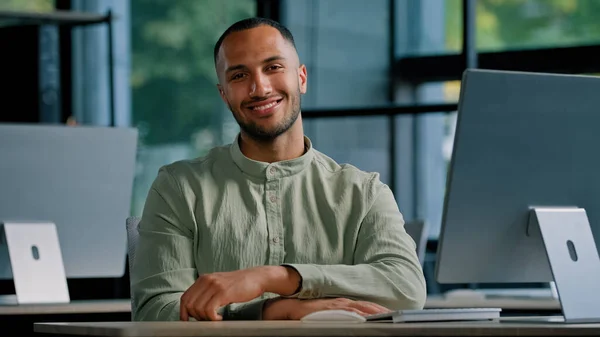 Happy smiling male investor multiracial worker developer programmer creative designer guy African American man with computer in office looking at camera smile sitting at table in company workplace
