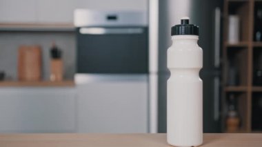Beyaz plastik spor şişesi su ile sıvı kalsiyum protein takviyesi mutfakta ahşap masanın üzerinde duran tanınmayan erkek sporcu Shaker 'ı alıp spor salonuna git.