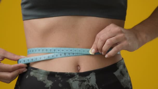 認識できない女の子の測定ウエストサイズ図体形状で測定テープチェック胃センチメートルダイエットフィットネススポーツワークアウト食事結果痩身重量損失でスタジオ黄色の背景 — ストック動画