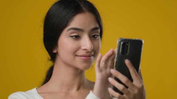 スタジオで閉じますポートレートインドの20代の女性の女性の女性は スマートフォンの画面を見てスクロール検索を入力インターネット上でチャットをオンラインチャット携帯電話と黄色の背景 — ストック動画