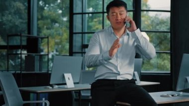 Asyalı iş adamı patron kurucu şirket 40 'lı yaşlarda orta yaşlı bir adam cep telefonundan arıyor cep telefonuyla 5G bağlantısı modern ofiste iş arkadaşlarıyla cep telefonu konuşmaları yapıyorlar.