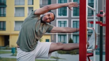 Güçlü Latin Amerikalı atletik adam yan eğik pozisyonda duruyor spor sahasındaki parmaklıklara eğiliyor sağlıklı vücut kasları ve spor konsepti için esnek egzersiz yapıyor.