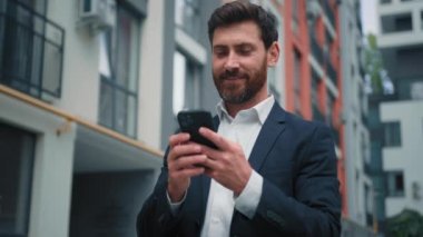 Çekici Kafkas işadamı kentte durmuş cep telefonuna mesaj atıyor olumlu gülümsüyor 30 'lu yılların serbest çalışanı internet dijital haber okuyor iyi bilgilendirme internette medya içeriğini tarıyor