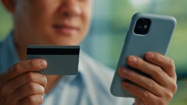 Erkek müşteri yetişkin Asyalı Japon işadamı mobil bankacılık uygulaması ile online ödeme yapıyor elektronik para transferi için kredi kartı kullanıyor güvenli ödemeler modern teknoloji uzaktan kolayca satın alınıyor