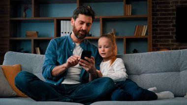 Mutlu aile kızı ve bekar baba modern aletlere bakın akıllı telefon videoları online internet iletişim kafkasyalı baba kızına cep telefonu ebeveyn kontrolünü kullanmayı öğretiyor.