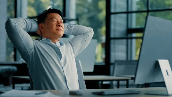 Asian korean senior businessman employee relaxing alone lean on office chair put hands behind head comfort rest feels satisfaction by computer work done take break after success deal working day off