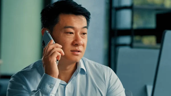 Sad Asian executive worker businessman manager middle-aged korean japanese chinese man answer mobile call work in office speak phone solve business problem distant conversation by 5g cell connection